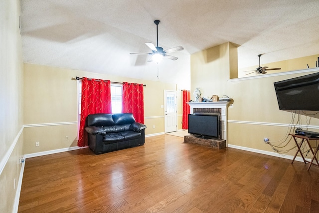 living area with a textured ceiling, a fireplace, wood finished floors, a ceiling fan, and vaulted ceiling