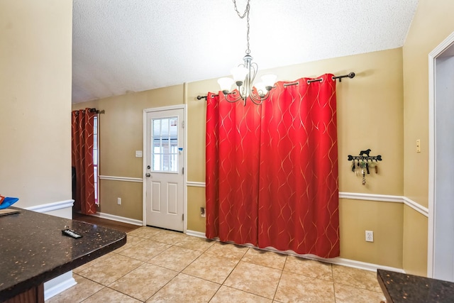 unfurnished dining area with baseboards, a textured ceiling, an inviting chandelier, and tile patterned floors