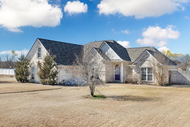 view of front of house with brick siding, roof with shingles, a front yard, and fence