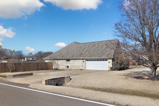 view of home's exterior featuring an attached garage, brick siding, a shingled roof, fence, and driveway