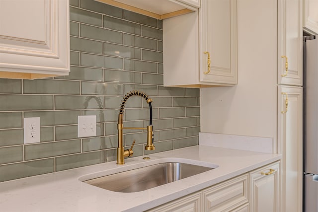 kitchen with cream cabinets, a sink, freestanding refrigerator, light stone countertops, and tasteful backsplash