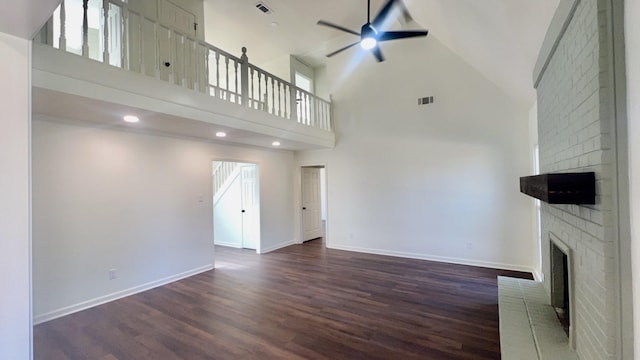 unfurnished living room with a brick fireplace, ceiling fan, visible vents, and wood finished floors