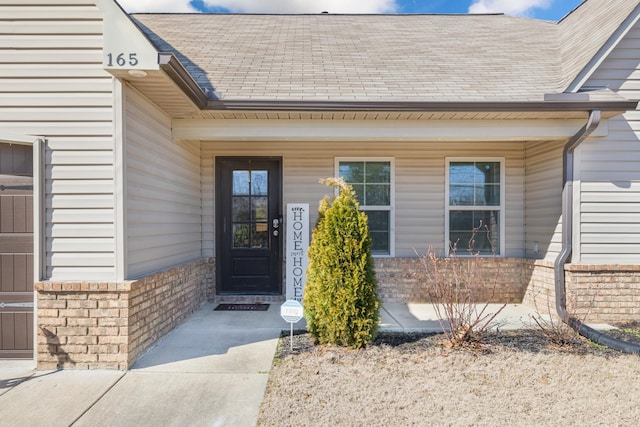 entrance to property with covered porch, roof with shingles, and brick siding