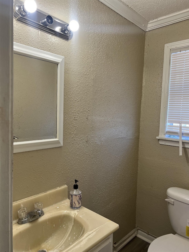 half bathroom with a textured ceiling, a textured wall, toilet, vanity, and ornamental molding