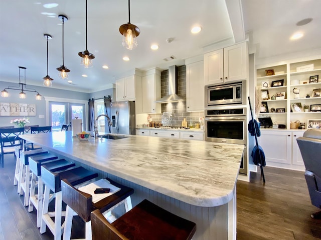 kitchen with stainless steel appliances, wall chimney range hood, a spacious island, and hanging light fixtures