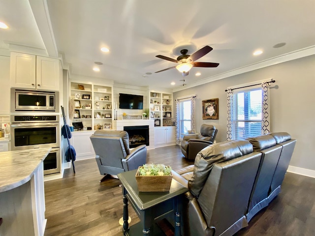 living room featuring a fireplace, a ceiling fan, baseboards, dark wood-style floors, and crown molding