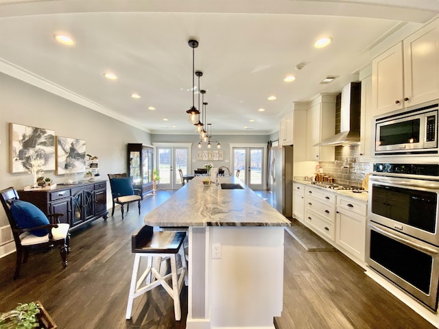 kitchen featuring stainless steel appliances, french doors, wall chimney range hood, and white cabinets