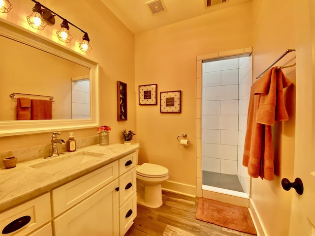 full bath featuring visible vents, tiled shower, toilet, wood finished floors, and vanity