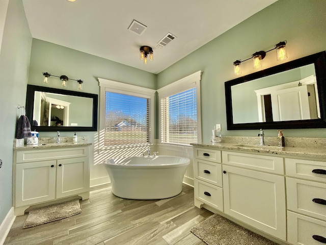 bathroom with wood finished floors, a freestanding tub, a sink, and visible vents