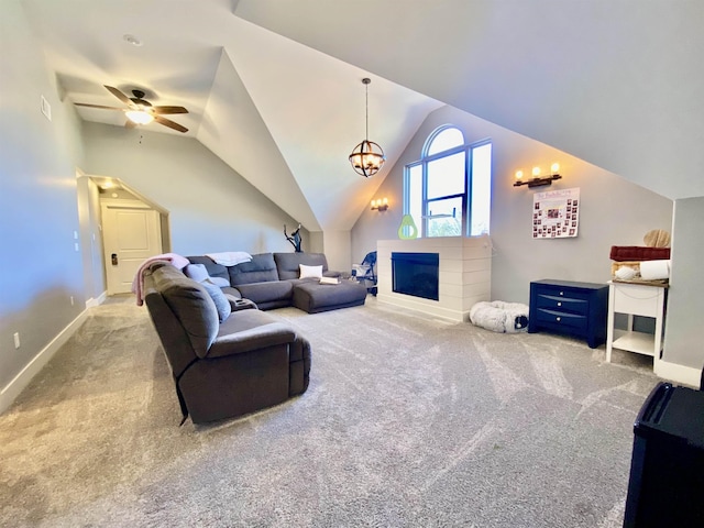 living room featuring light colored carpet, ceiling fan with notable chandelier, a fireplace, baseboards, and vaulted ceiling