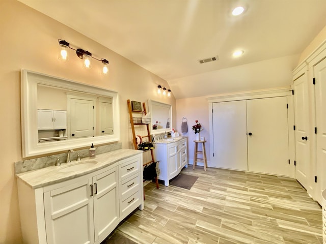 full bath featuring visible vents, vaulted ceiling, a sink, and wood finished floors