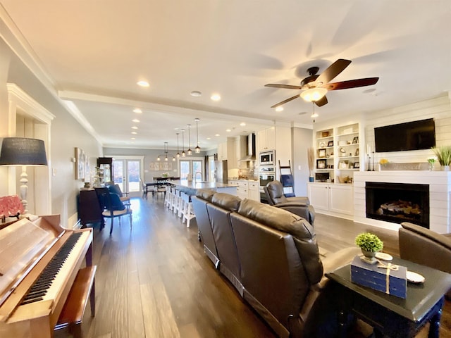 living room with built in features, dark wood-style floors, ceiling fan, a fireplace, and recessed lighting