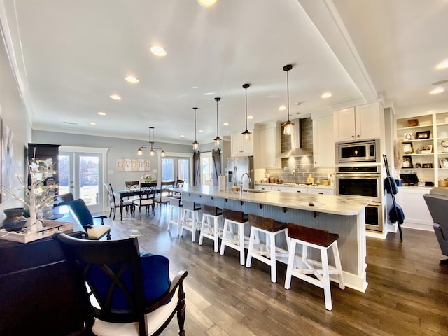 kitchen featuring hanging light fixtures, wall chimney exhaust hood, a large island, and white cabinets