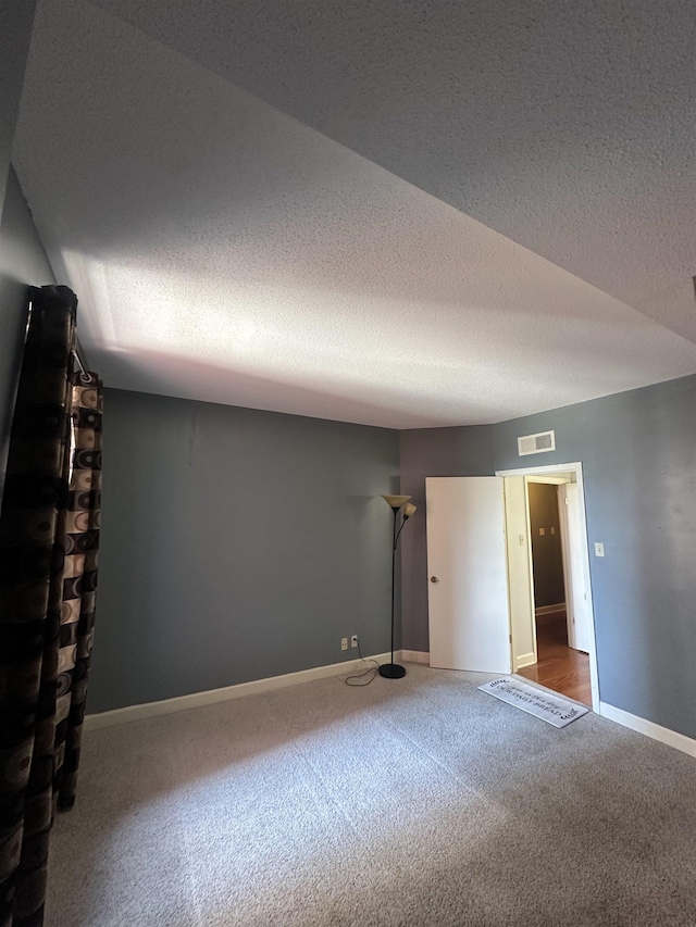 carpeted empty room featuring a textured ceiling, visible vents, and baseboards