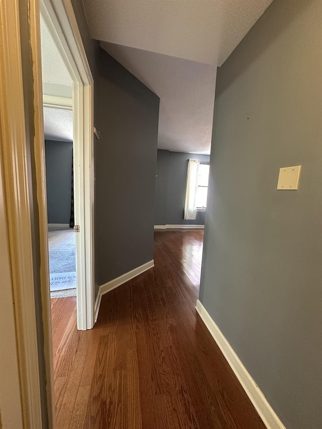 corridor featuring dark wood-style flooring, a textured ceiling, and baseboards