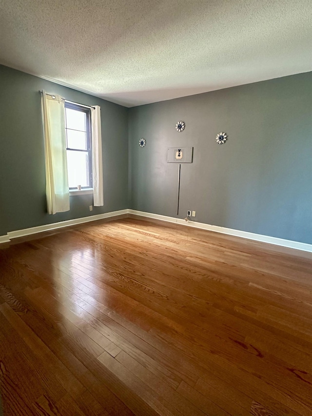 unfurnished room featuring a textured ceiling, wood finished floors, and baseboards