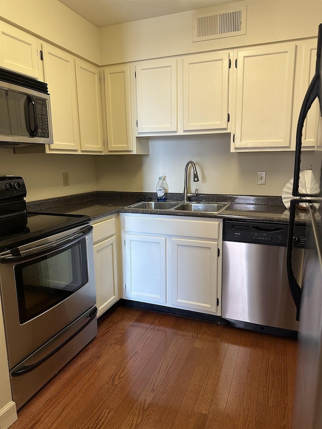 kitchen featuring stainless steel appliances, a sink, visible vents, white cabinetry, and dark countertops