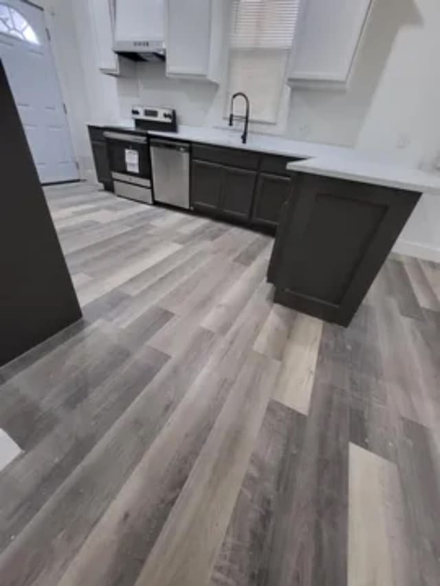 kitchen with light wood finished floors, light countertops, appliances with stainless steel finishes, white cabinetry, and a sink