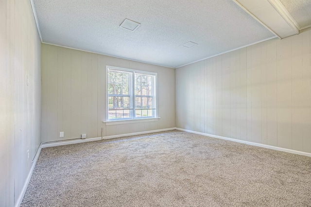 carpeted spare room with a textured ceiling, ornamental molding, and baseboards