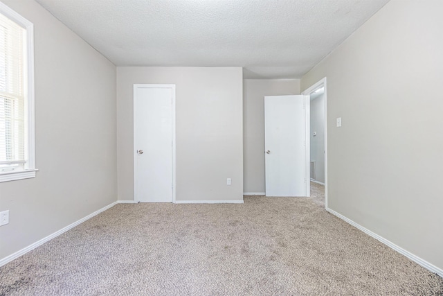 unfurnished bedroom with a textured ceiling, a closet, baseboards, and light colored carpet