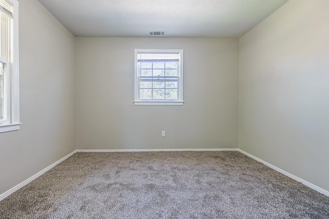 empty room with a textured ceiling, carpet, visible vents, and baseboards