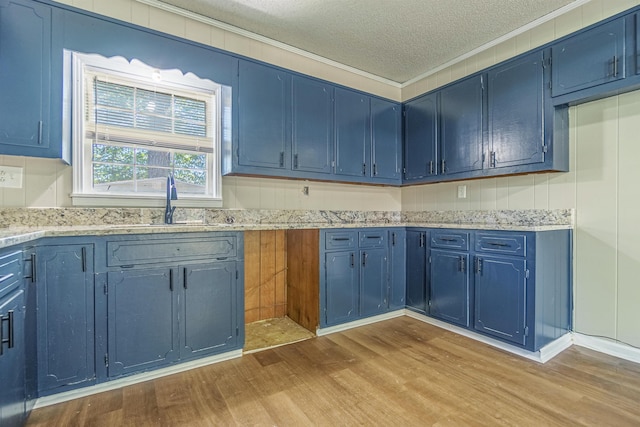 kitchen with blue cabinets, light stone countertops, light wood-style flooring, and crown molding