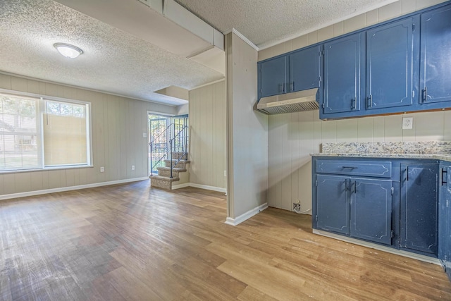 kitchen with light wood-style floors, under cabinet range hood, light stone counters, and blue cabinetry