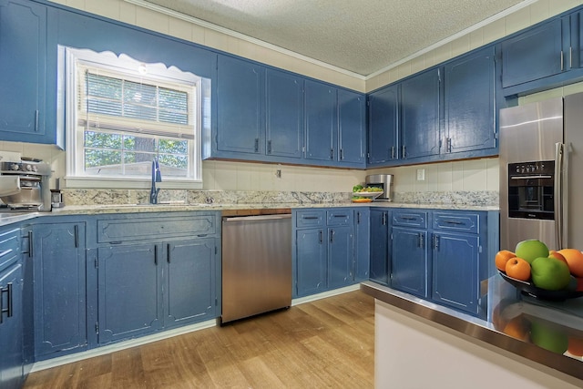 kitchen with blue cabinetry, ornamental molding, stainless steel appliances, and light wood-style floors