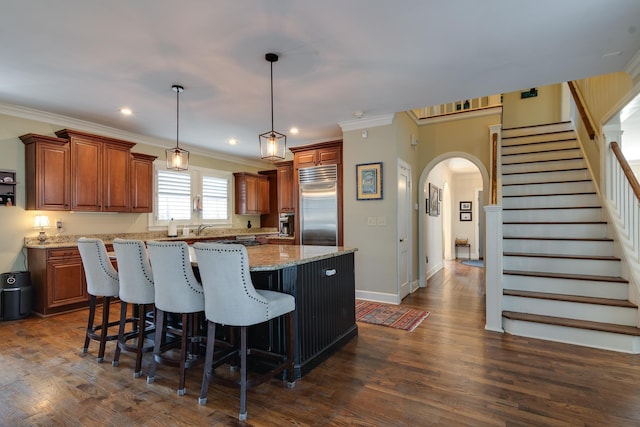 kitchen with arched walkways, light stone counters, a center island, built in refrigerator, and hanging light fixtures