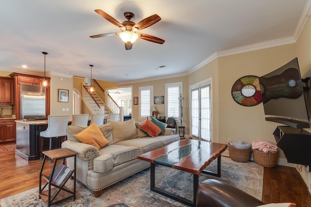 living area with wood finished floors, visible vents, a ceiling fan, ornamental molding, and stairway