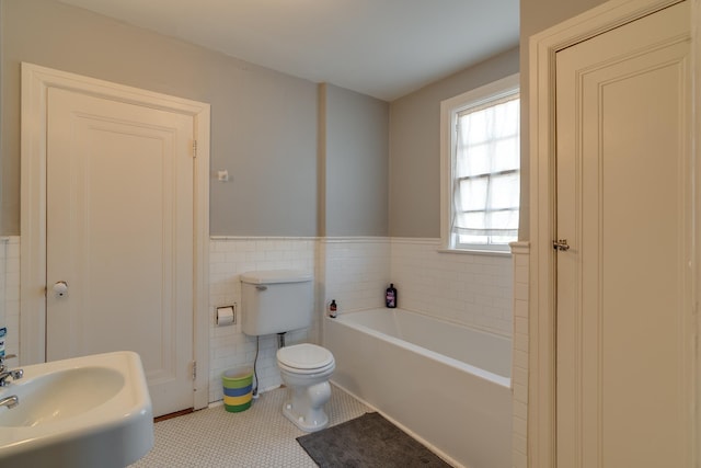 bathroom with tile patterned flooring, toilet, tile walls, wainscoting, and a bath