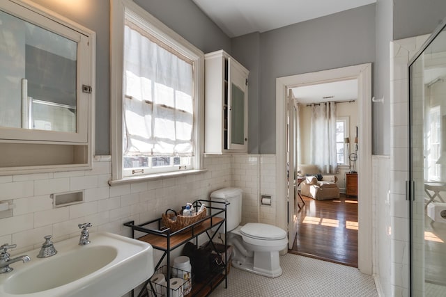 bathroom featuring tile patterned flooring, a sink, tile walls, wainscoting, and a stall shower