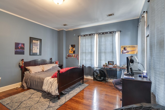 bedroom featuring baseboards, visible vents, wood finished floors, and ornamental molding