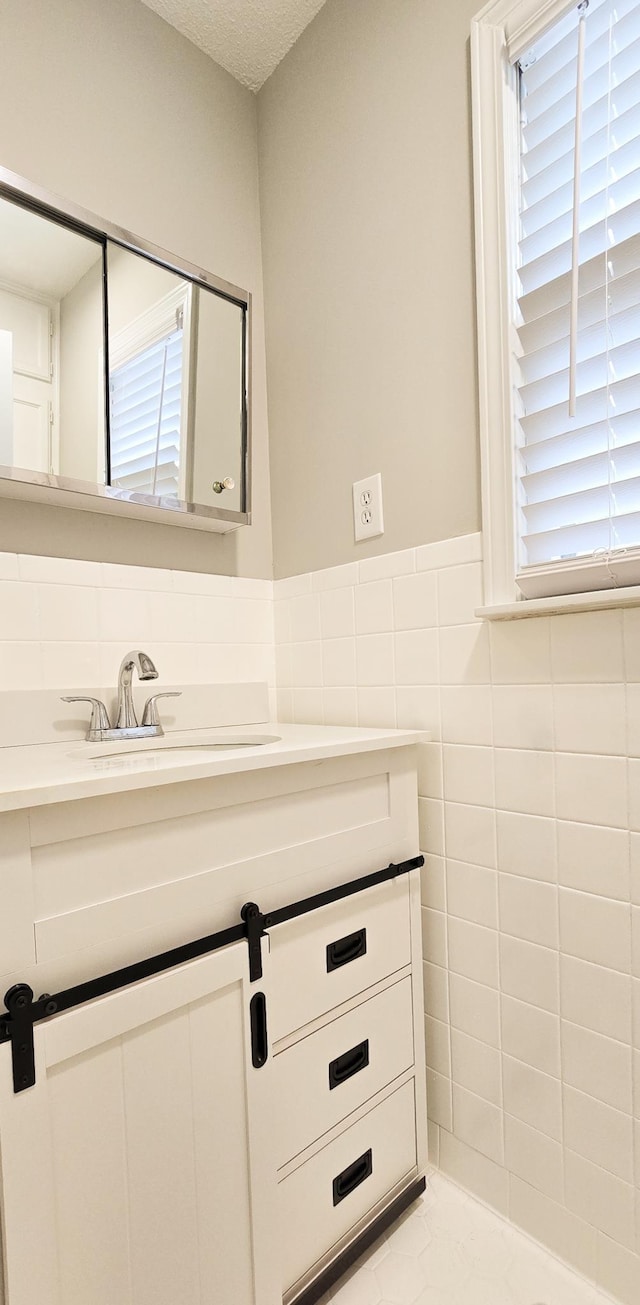 bathroom featuring a textured ceiling, vanity, tile walls, and wainscoting