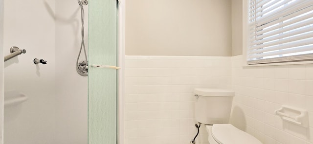 full bathroom featuring toilet, a shower with shower door, wainscoting, and tile walls