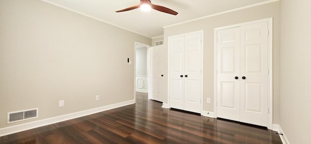 unfurnished bedroom with multiple closets, visible vents, crown molding, and dark wood-style floors