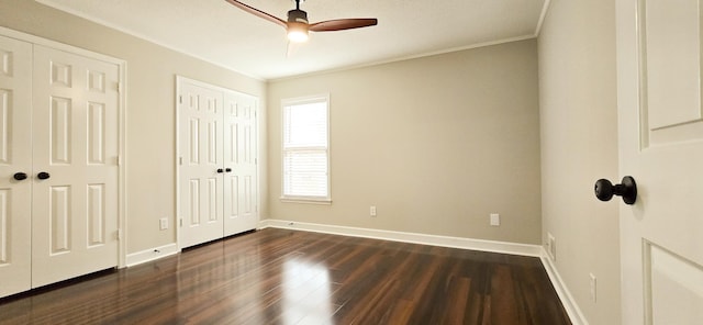 unfurnished bedroom with dark wood-style flooring, two closets, ornamental molding, ceiling fan, and baseboards