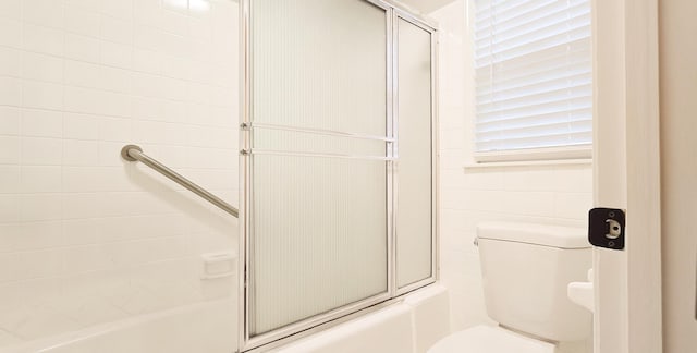 bathroom with toilet, combined bath / shower with glass door, and tile walls