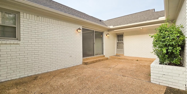 property entrance with roof with shingles, a patio, and brick siding