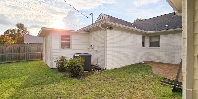 view of side of property featuring a shingled roof, fence, a yard, central AC, and brick siding