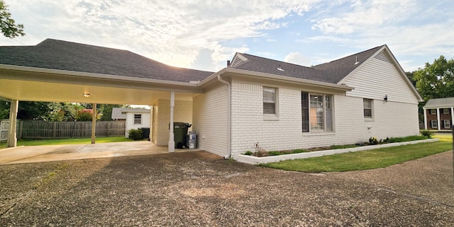 view of side of home featuring concrete driveway, brick siding, a shingled roof, and fence