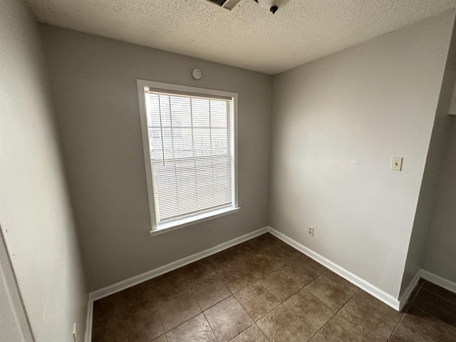 spare room with a healthy amount of sunlight, a textured ceiling, baseboards, and dark tile patterned floors