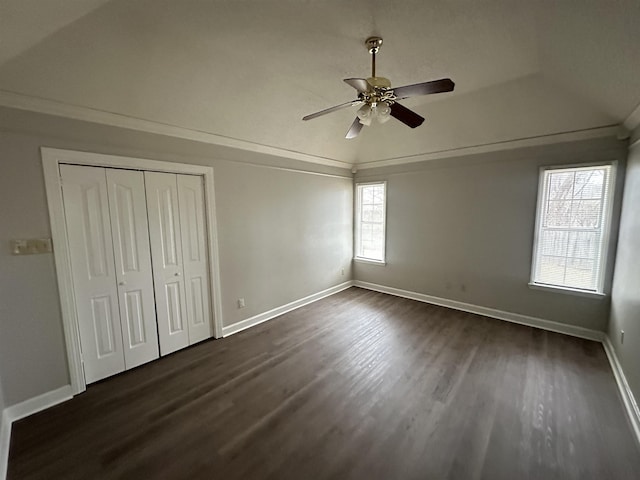 unfurnished bedroom featuring baseboards, dark wood-style floors, ceiling fan, crown molding, and a closet