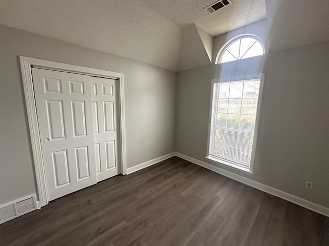 unfurnished bedroom featuring a textured ceiling, dark wood-style flooring, visible vents, and baseboards