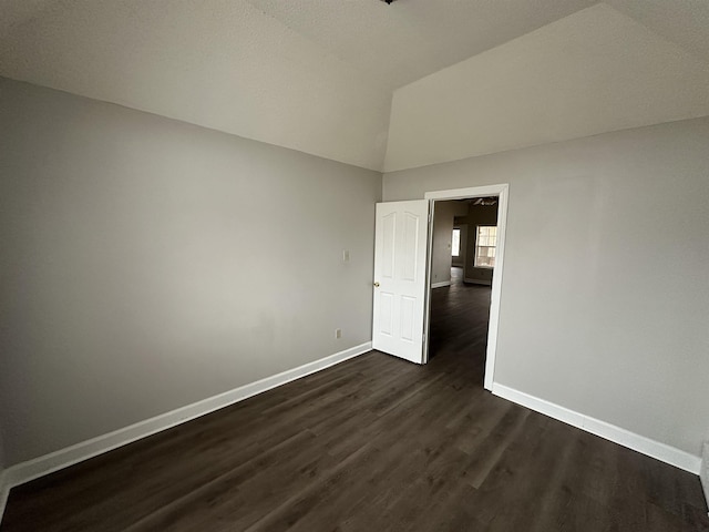 unfurnished room with vaulted ceiling, dark wood finished floors, and baseboards