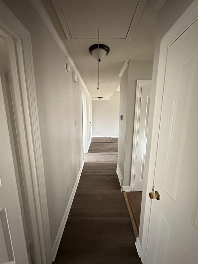 corridor featuring dark wood-style floors, attic access, baseboards, and crown molding