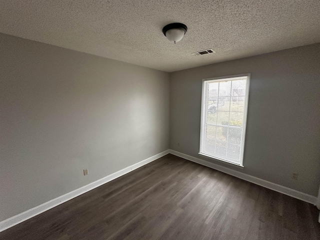 empty room featuring a textured ceiling, dark wood-style flooring, visible vents, and baseboards