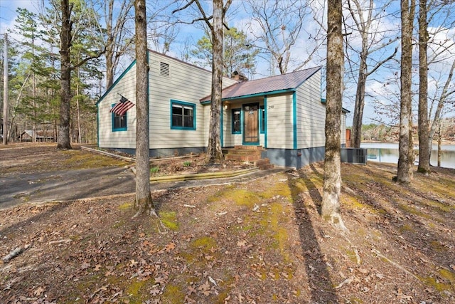 view of front facade featuring a water view, a chimney, central AC unit, and metal roof