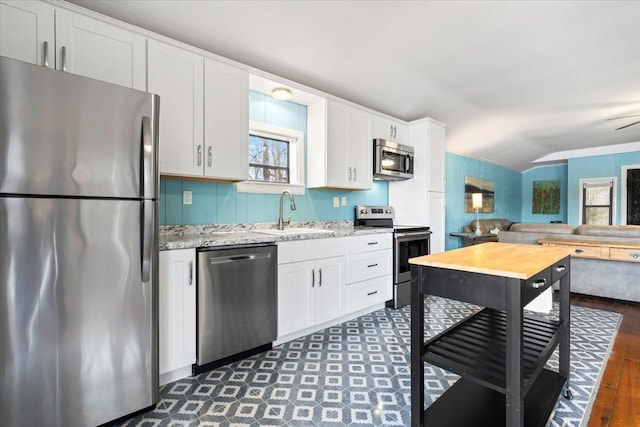 kitchen with appliances with stainless steel finishes, open floor plan, light stone countertops, white cabinetry, and a sink