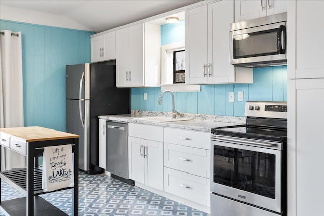 kitchen featuring lofted ceiling, wooden walls, stainless steel appliances, a sink, and white cabinets